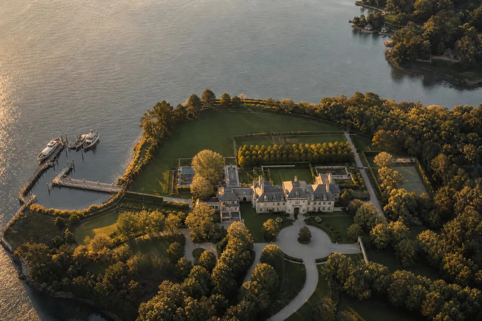 Aerial view of a waterfront estate with manicured grounds and moored boats at dusk.