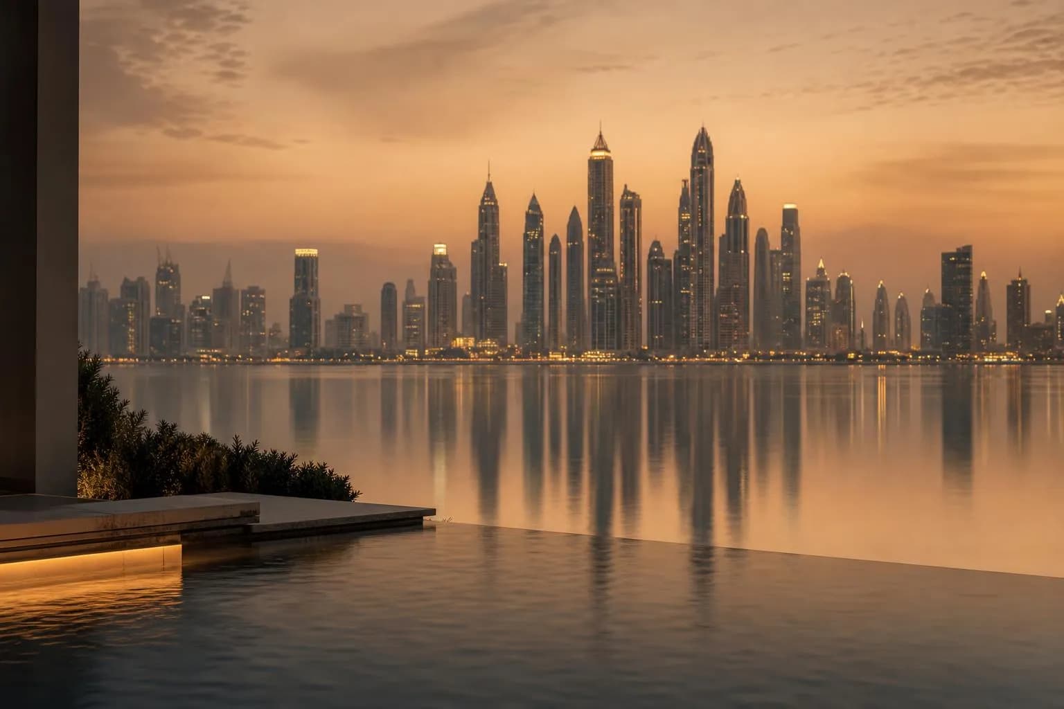 City skyline glowing at dusk across still, reflective water under a deepening sky.