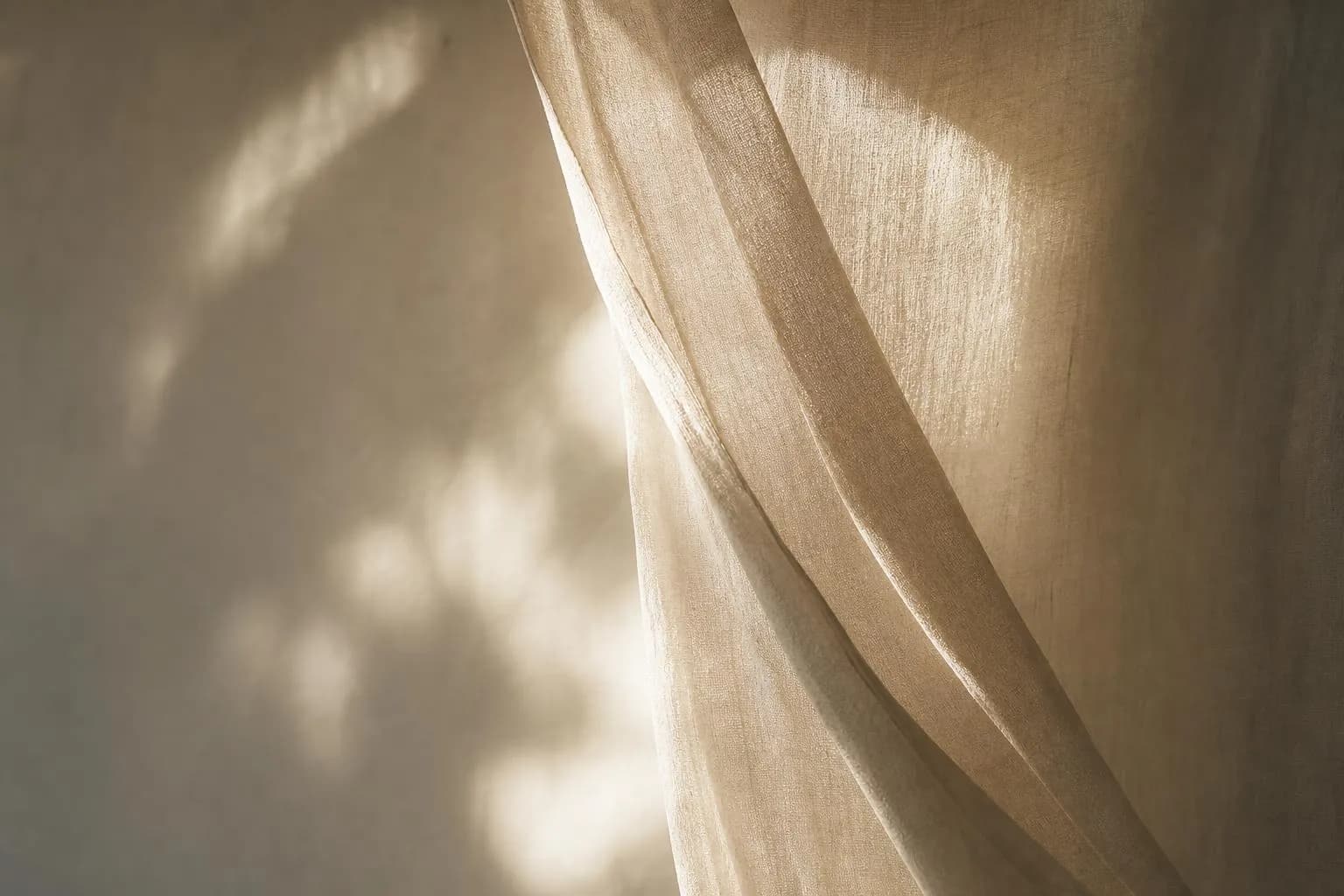 Soft sunlight filtering through translucent linen, casting gentle shadows on a plain wall.