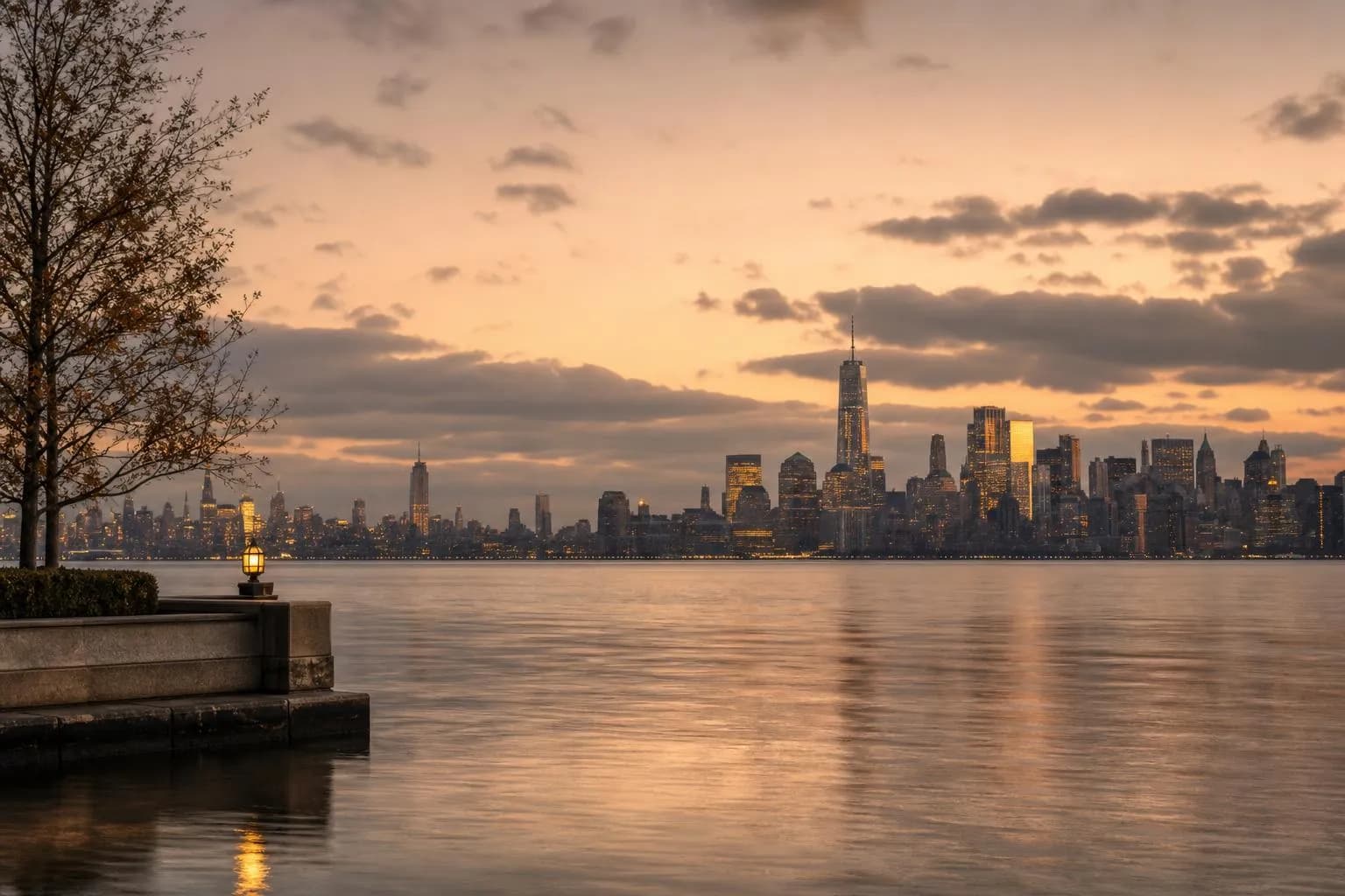 Distant city skyline at dusk reflected in calm water, warm light on residential buildings