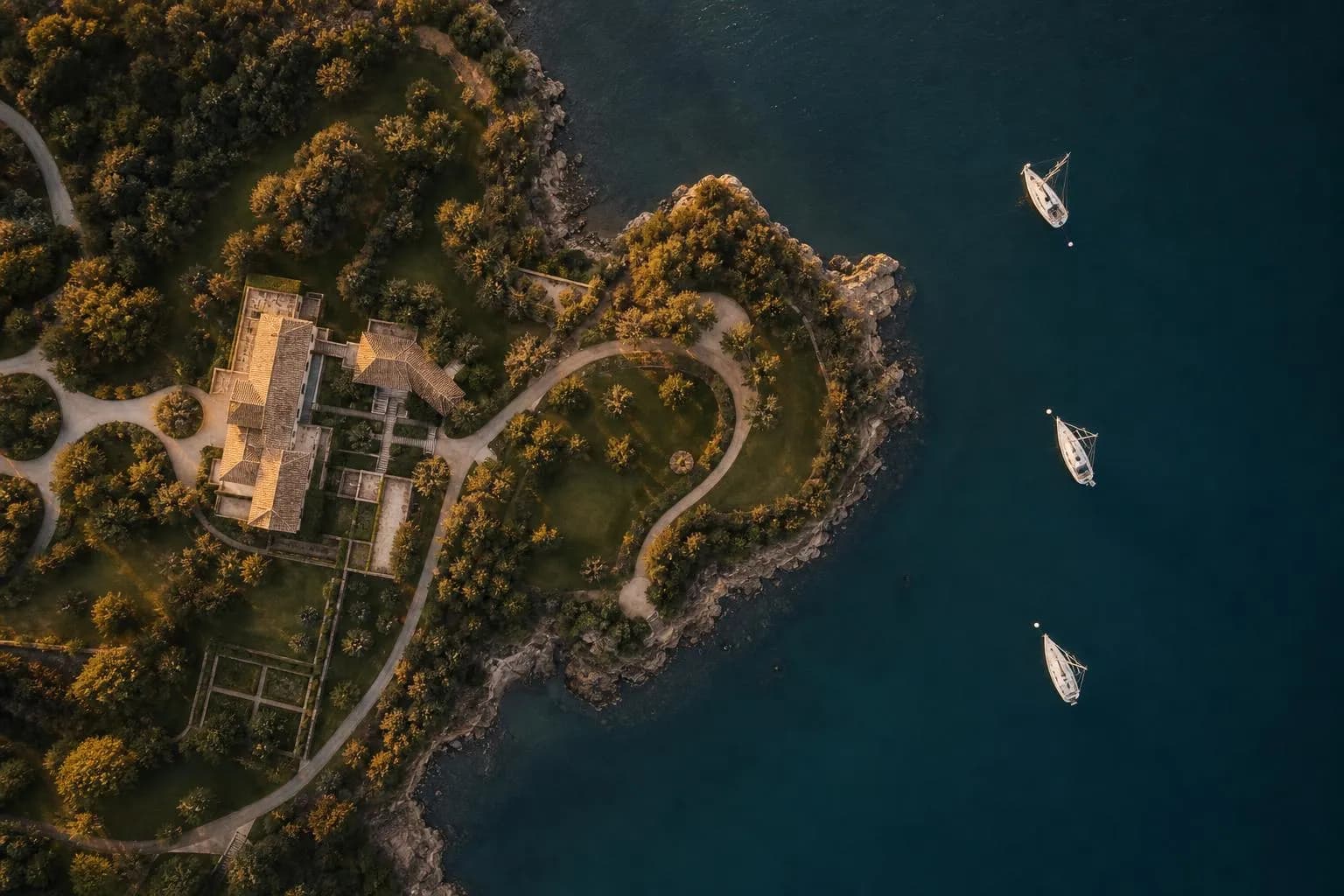 Overhead aerial view of a refined coastal estate with moored boats and manicured grounds at sunset.