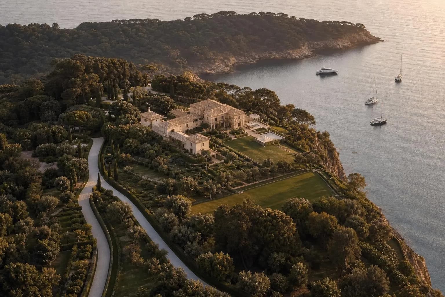 Aerial view of a coastal estate with private drive, manicured grounds, and moored boats below.