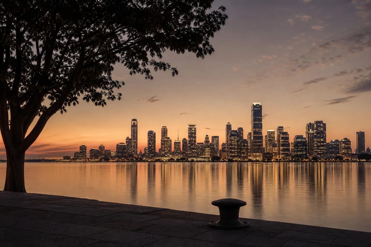 Distant city skyline reflected in still water at dusk, viewed from a quiet waterfront.
