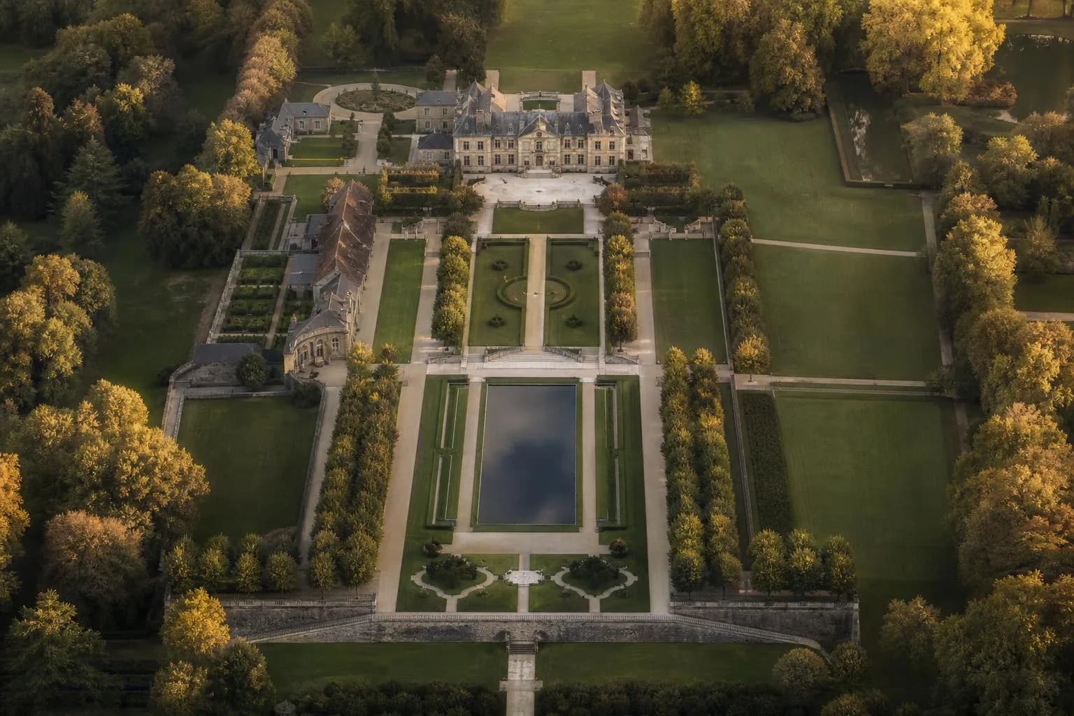 Aerial view of a manicured estate with geometric garden patterns and pathways at golden hour.