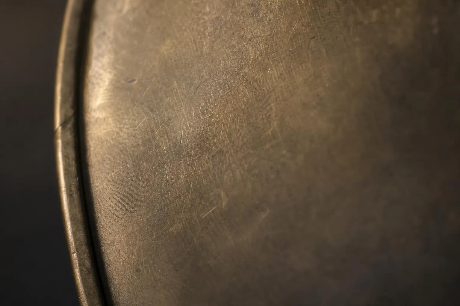 Close-up of textured brass surface with patina and wear marks in dramatic side-lighting.