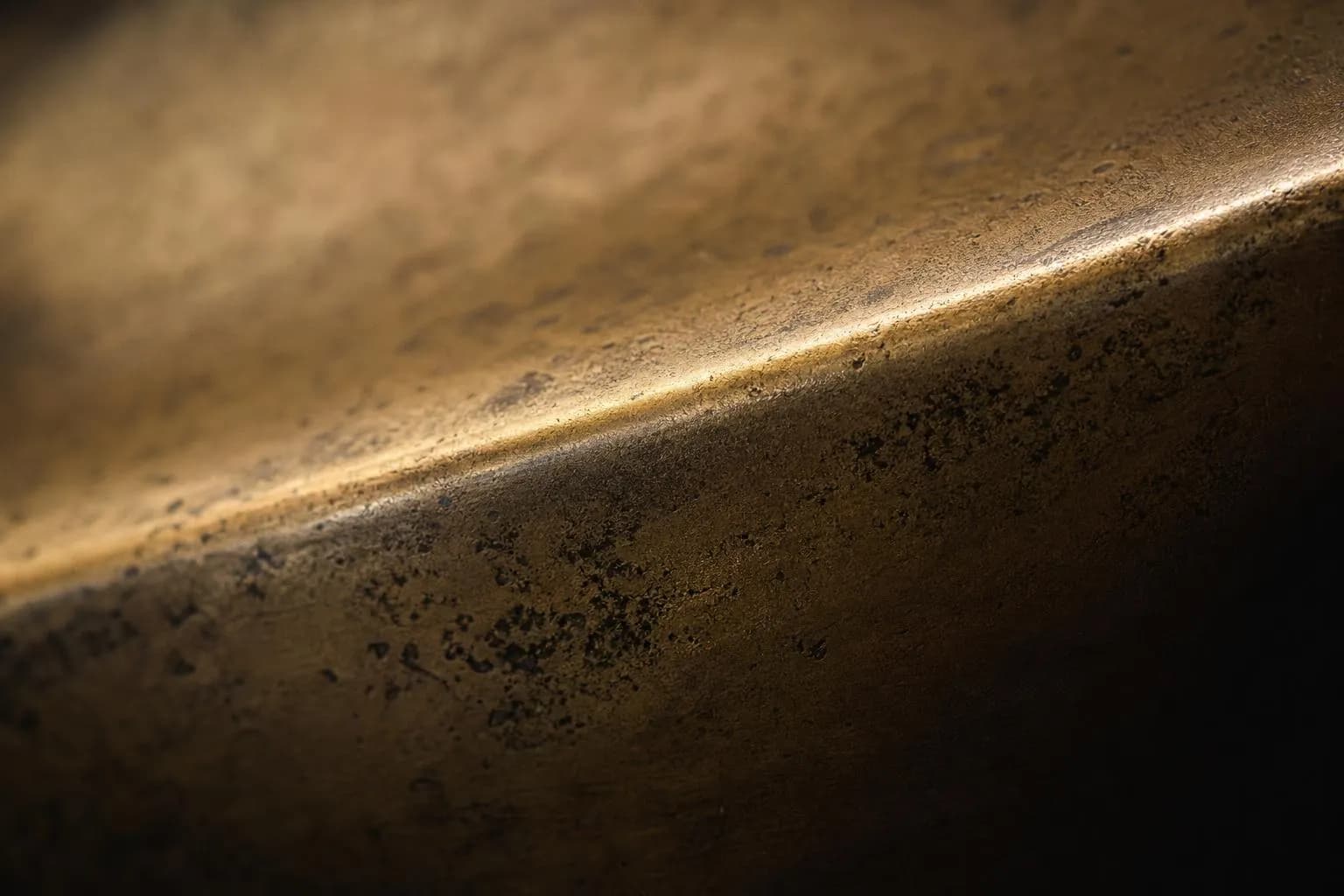 Close-up of textured brass surface with patina and light raking across fine details.