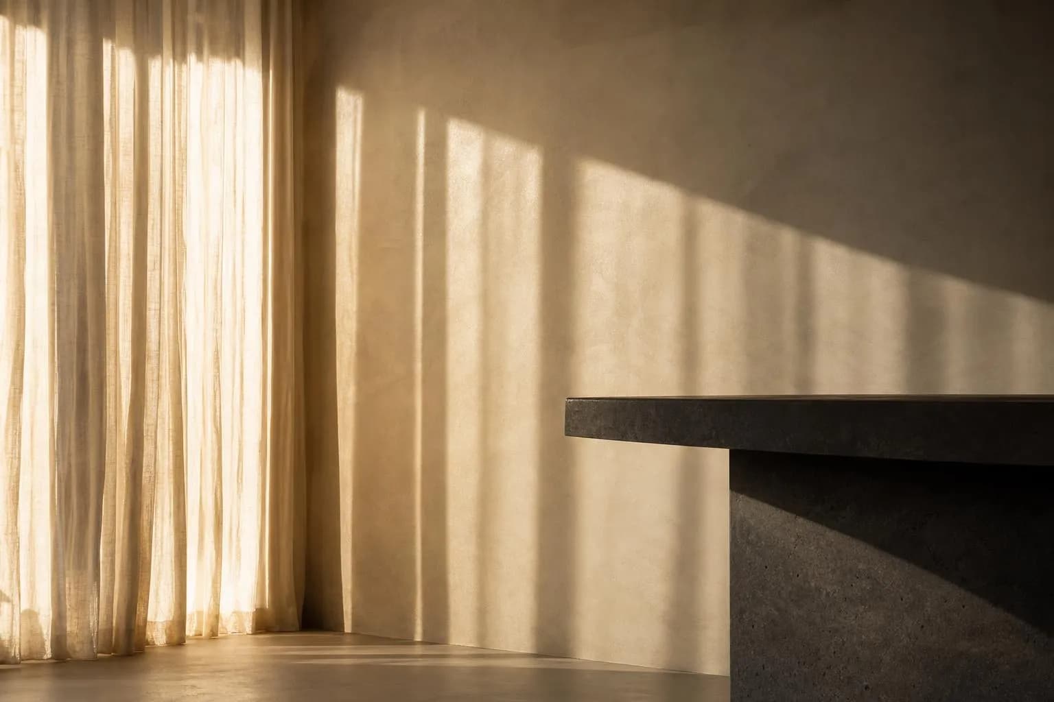 Minimalist interior with filtered sunlight casting soft shadows on a pale wall through sheer curtains.