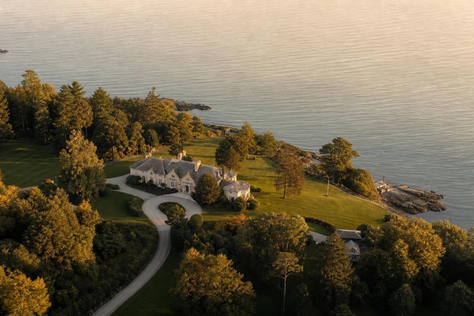 Aerial view of a coastal estate with manicured grounds and private drive at sunset.