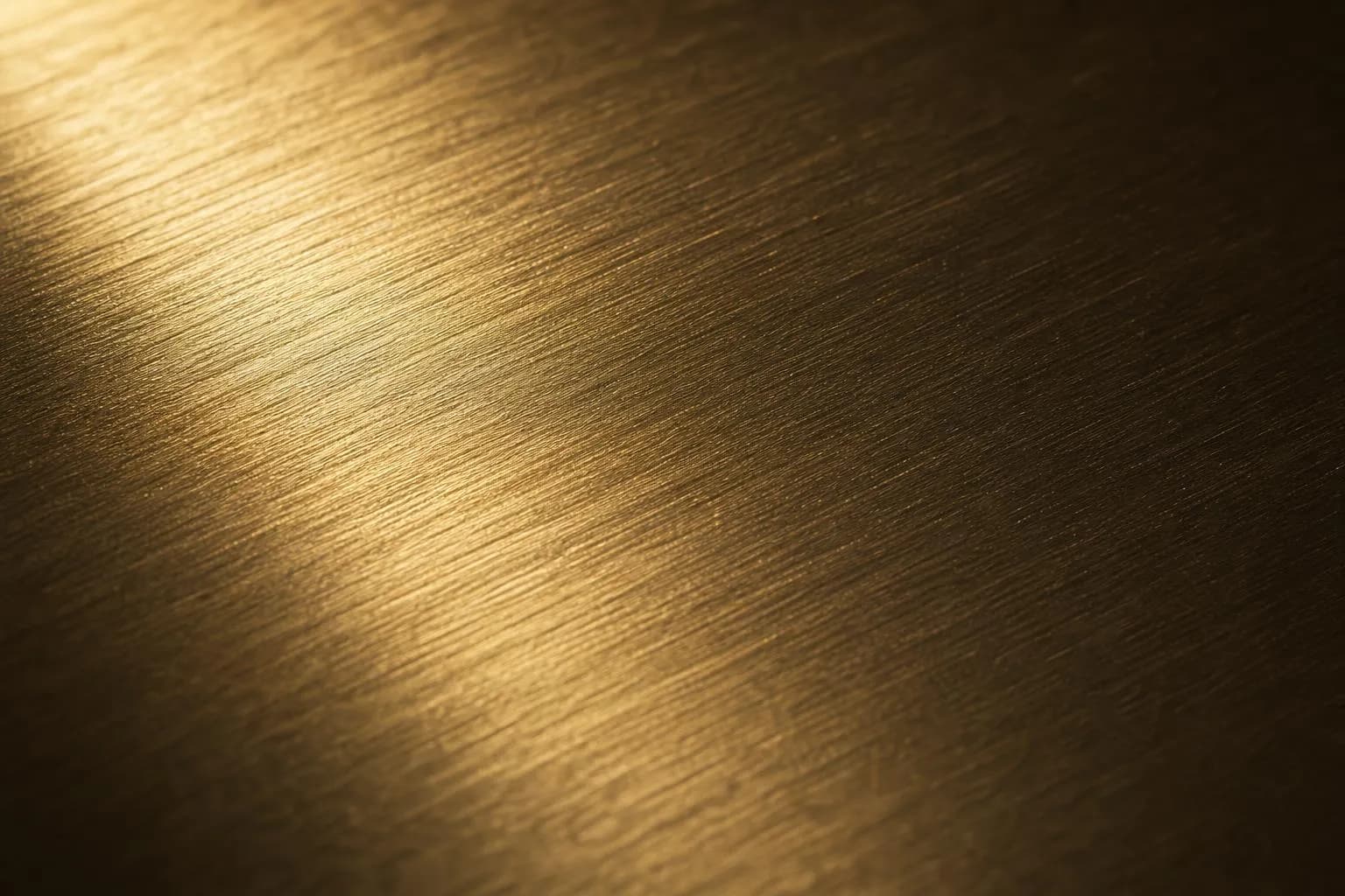 Close-up of brushed brass or bronze surface with raking light revealing fine linear texture and dimensional quality.