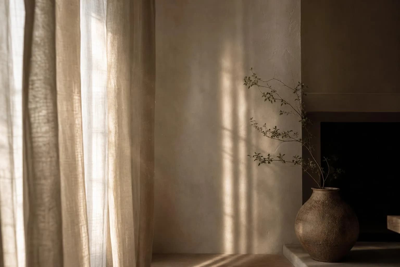 Sunlight through sheer curtains casting soft shadows on a pale wall, evoking stillness and contemplation.