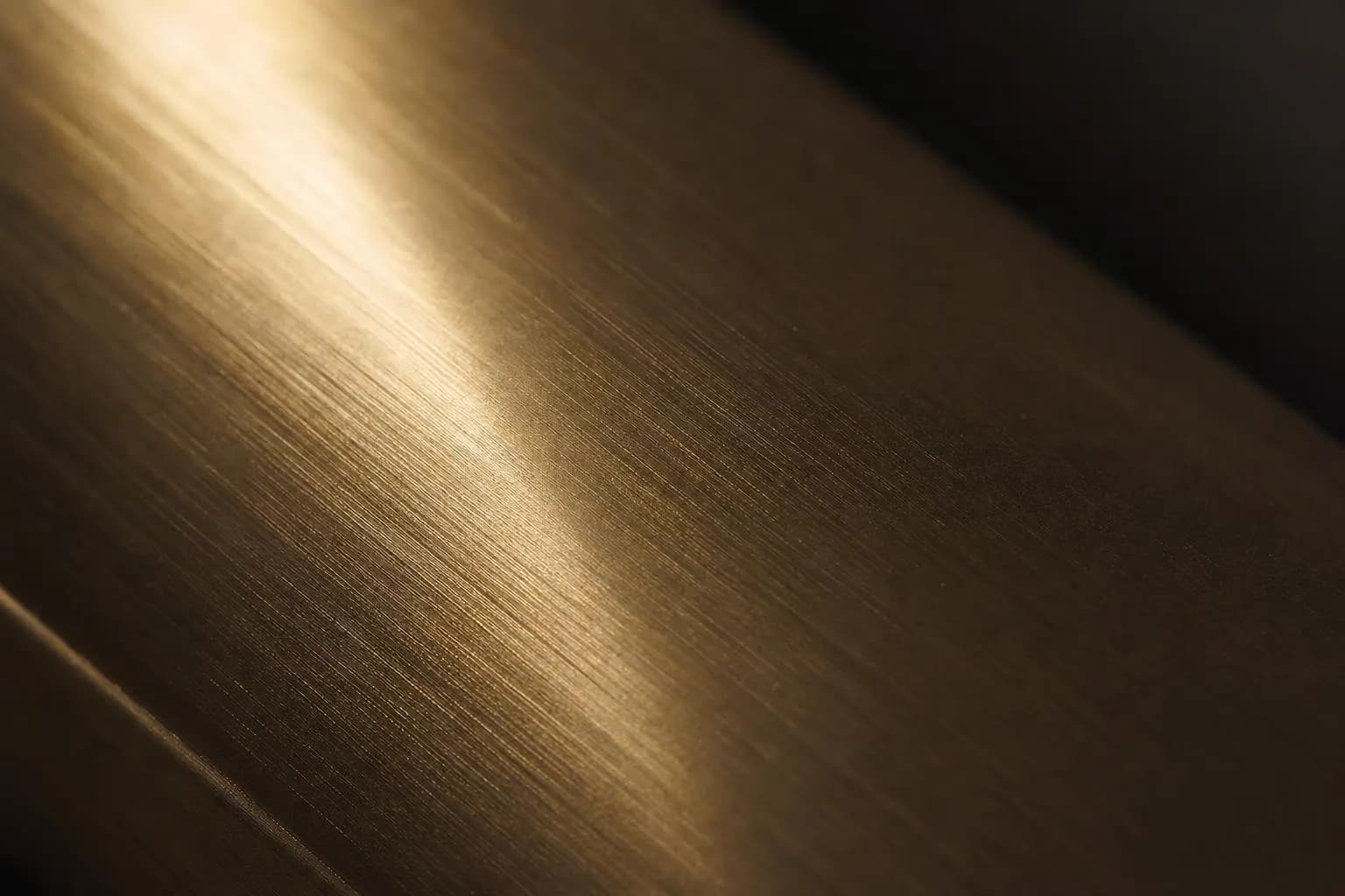 Extreme close-up of brushed brass surface with precise linear texture and selective light.