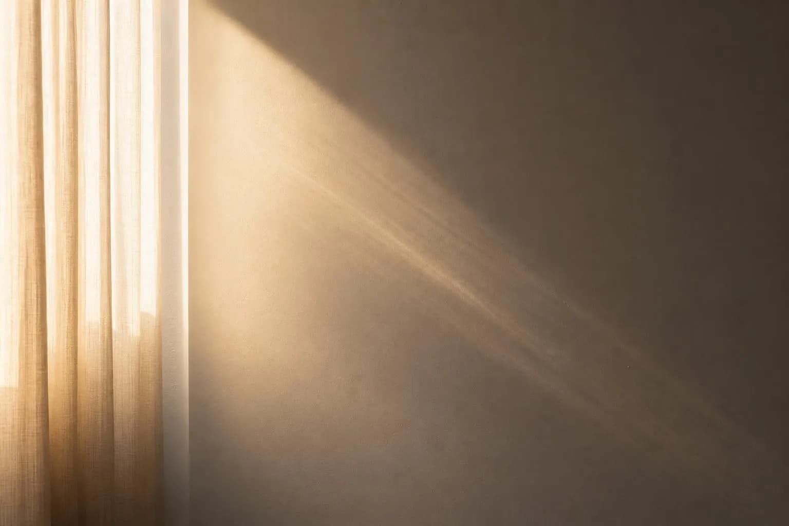 Sunlight filtering through sheer curtains onto a minimalist white wall, creating subtle shadow gradients.