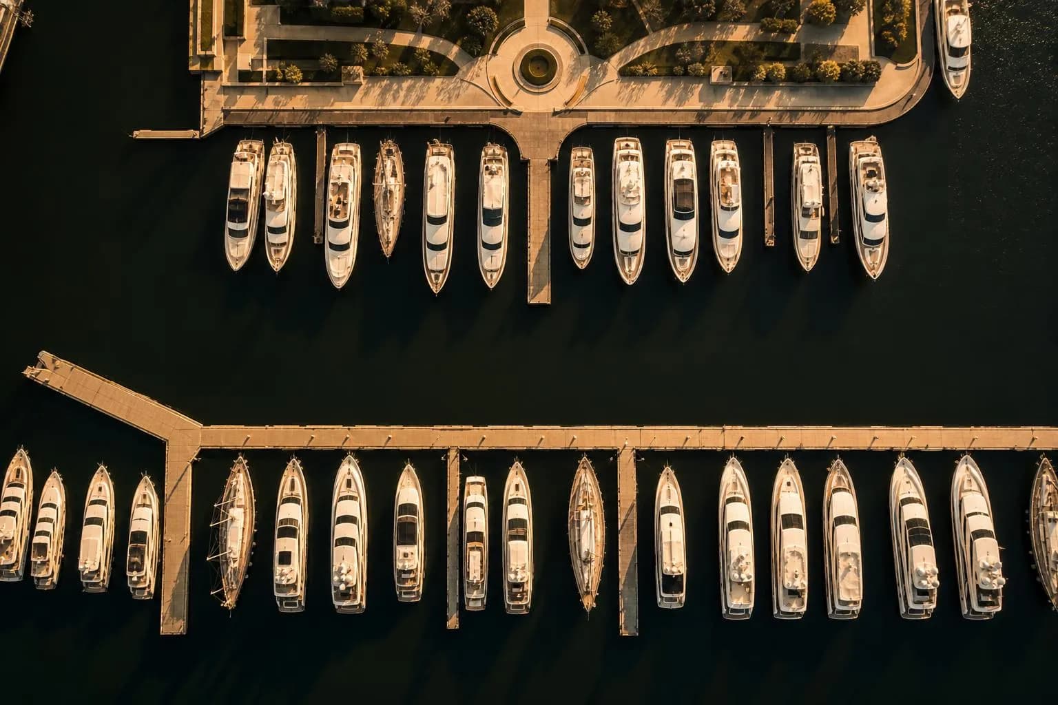 Overhead view of moored yachts in a private marina at sunset, arranged in orderly rows.
