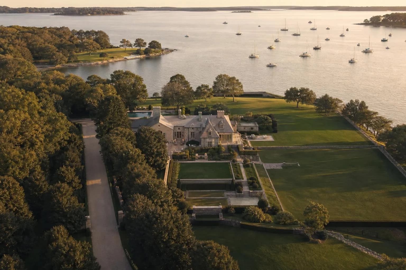 Aerial view of an elegant coastal estate with manicured grounds and private marina at sunset.