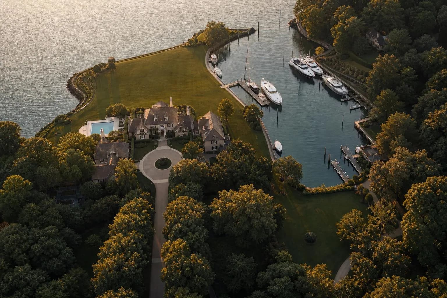 Aerial view of a private waterfront estate with gardens, driveway, and moored boats at sunset.