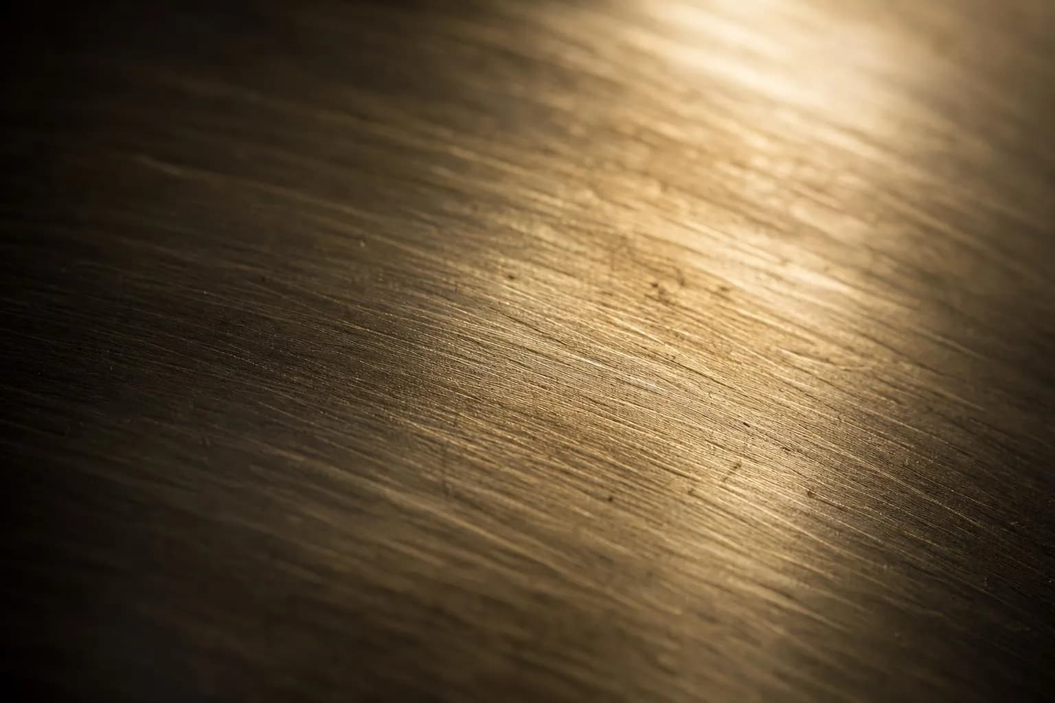Close-up of brushed brass surface with raking light revealing fine texture and patina variation.