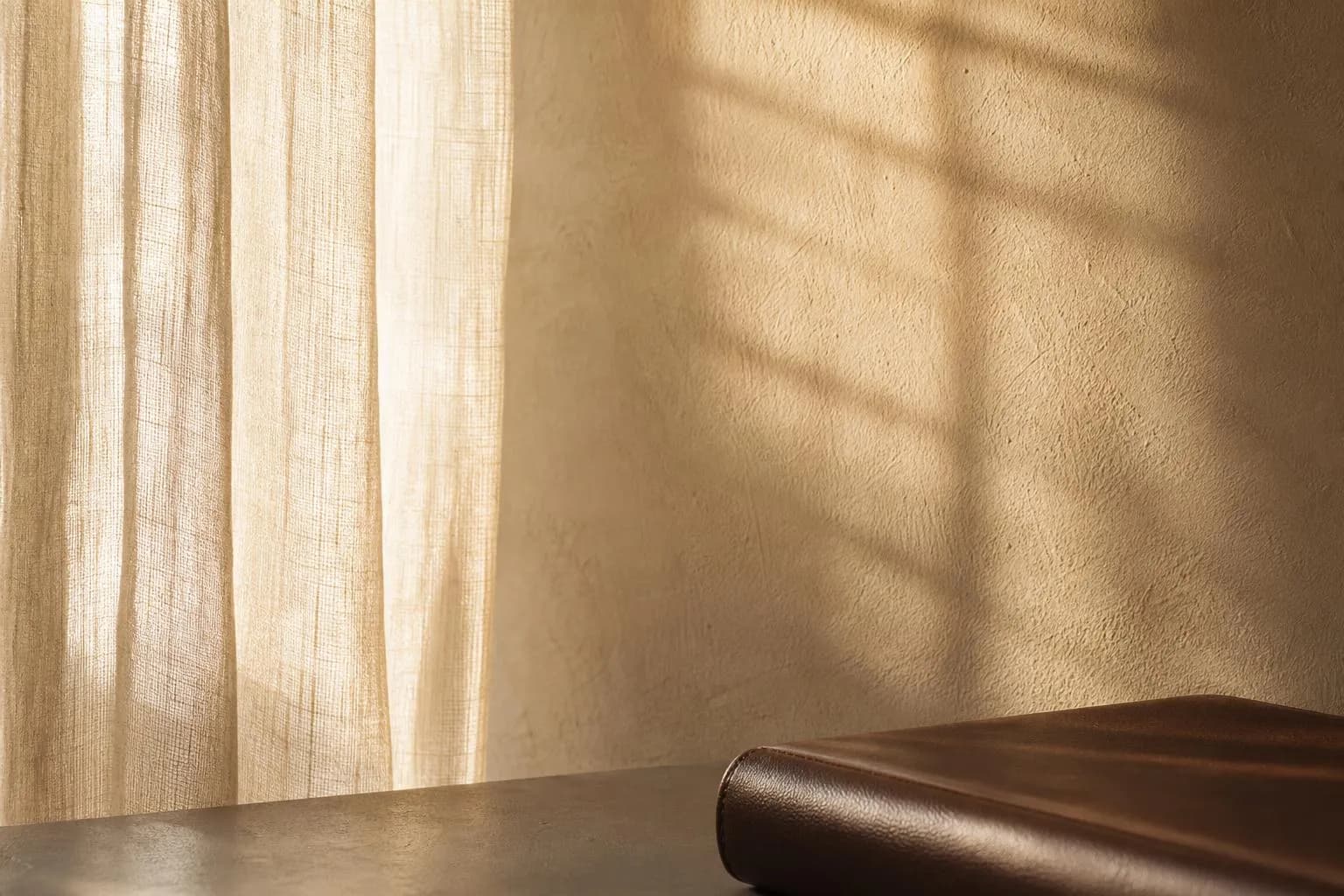 Sunlight filters through sheer fabric onto a textured wall, casting soft shadows.