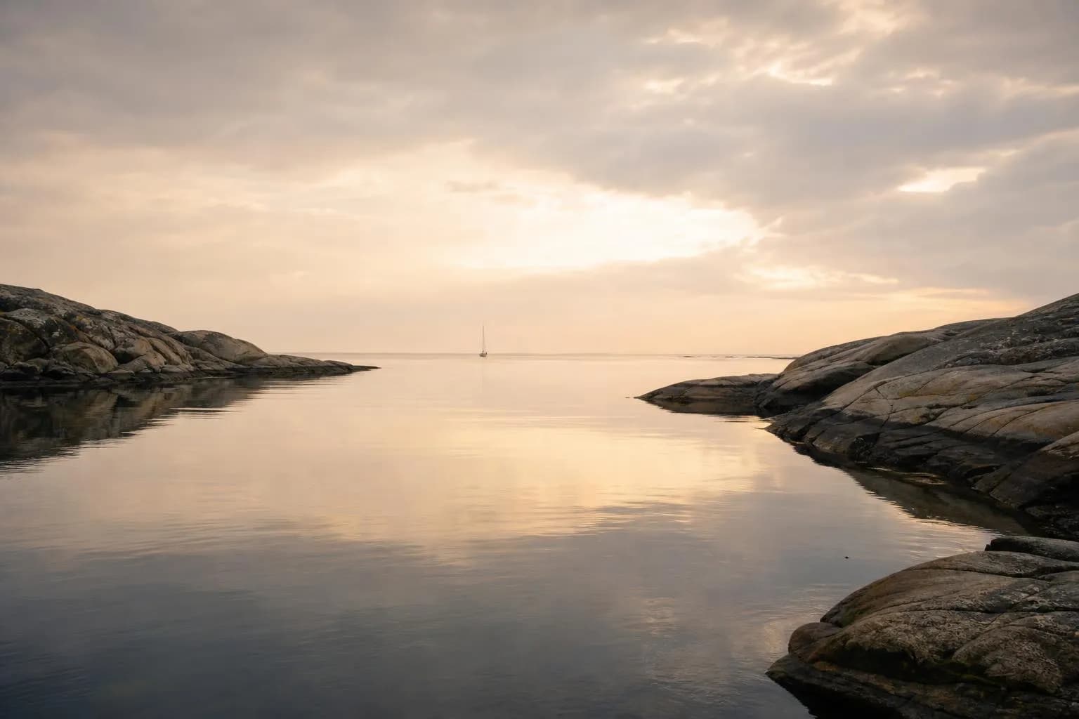 Serene coastal dawn with calm water, distant sailboat, and rocky headlands in soft light