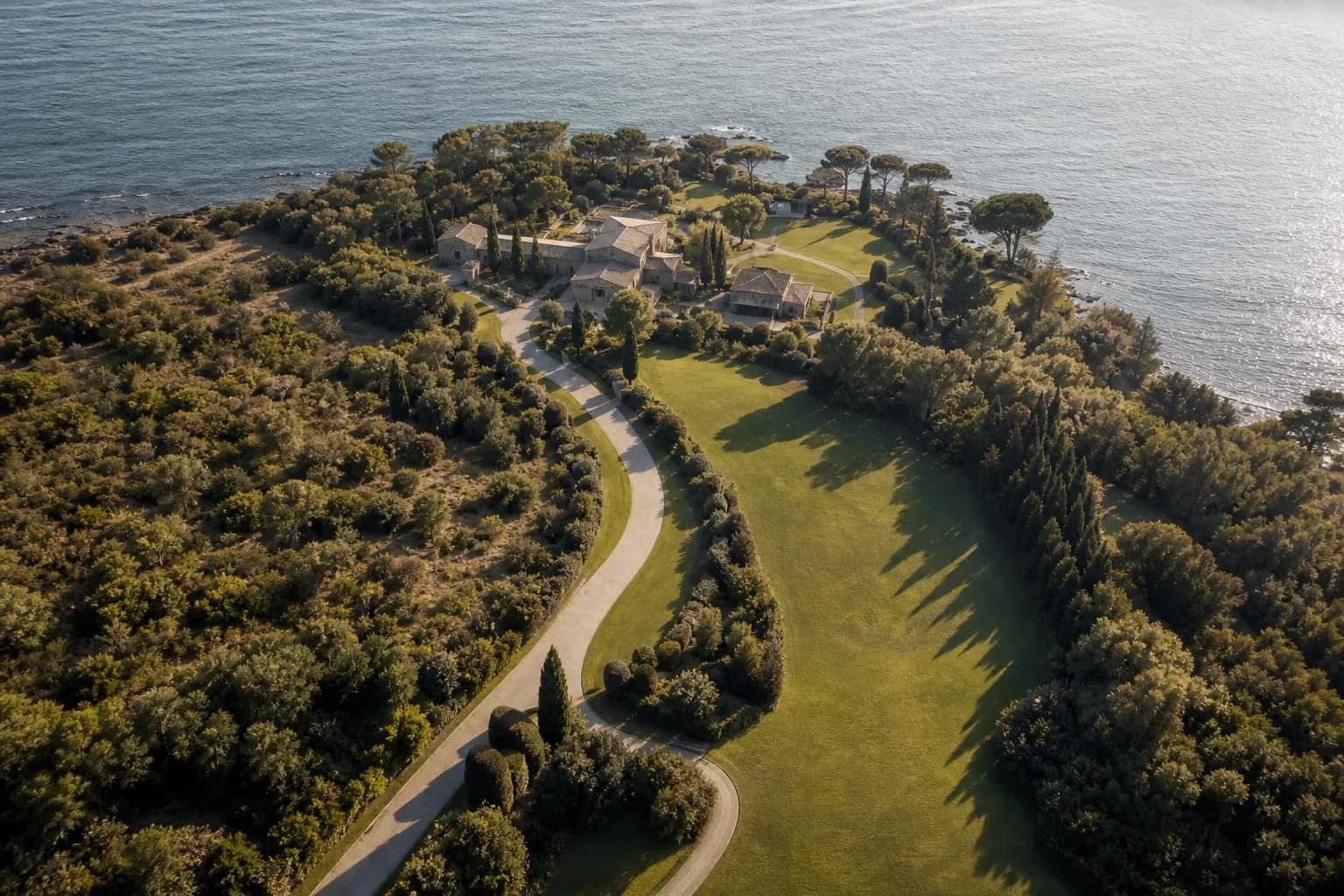 Aerial view of a manicured coastal estate with winding drive and waterfront property in soft afternoon light