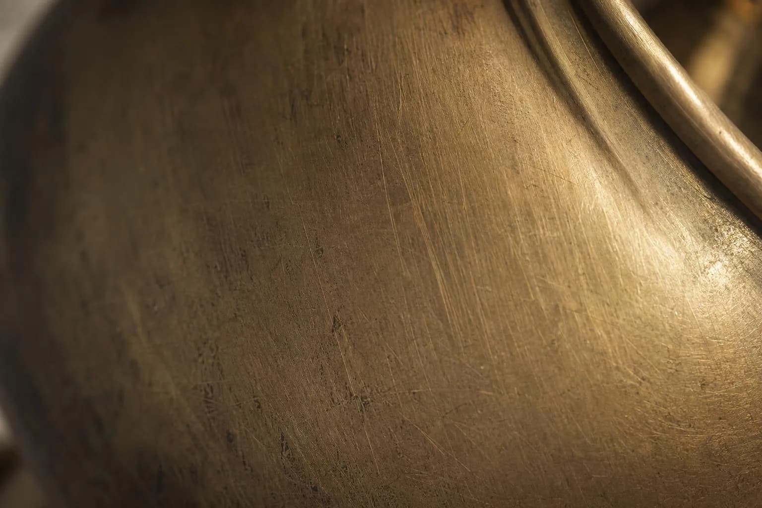 Close-up of aged brushed brass surface with fine texture and patina, lit by directional light