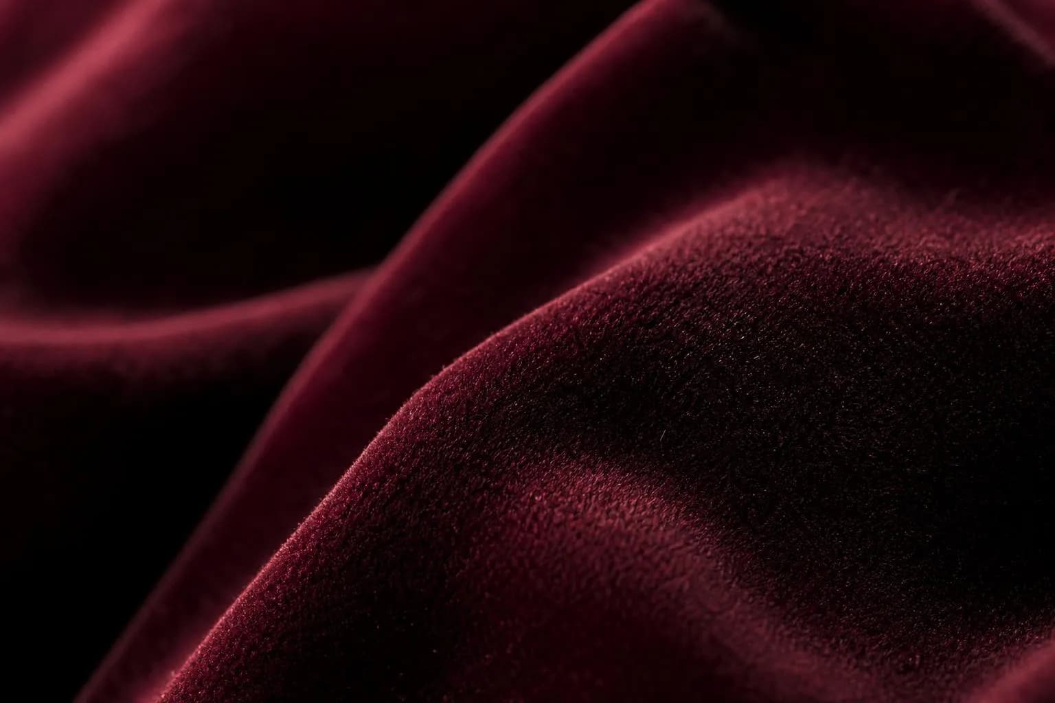 Close-up of burgundy velvet fabric with rich texture and subtle sheen under warm sidelight