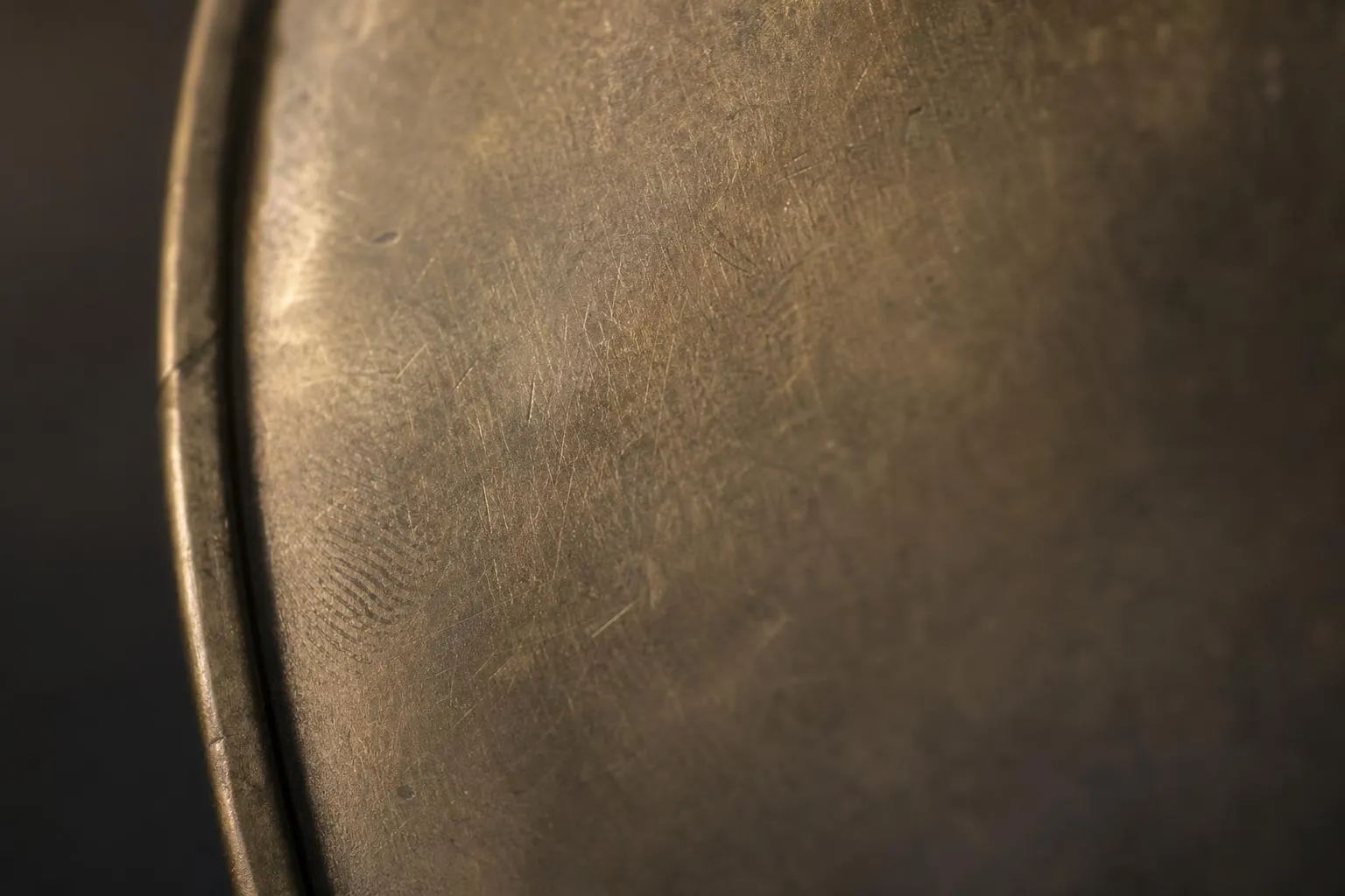 Close-up of textured brass surface with patina and wear marks in dramatic side-lighting.