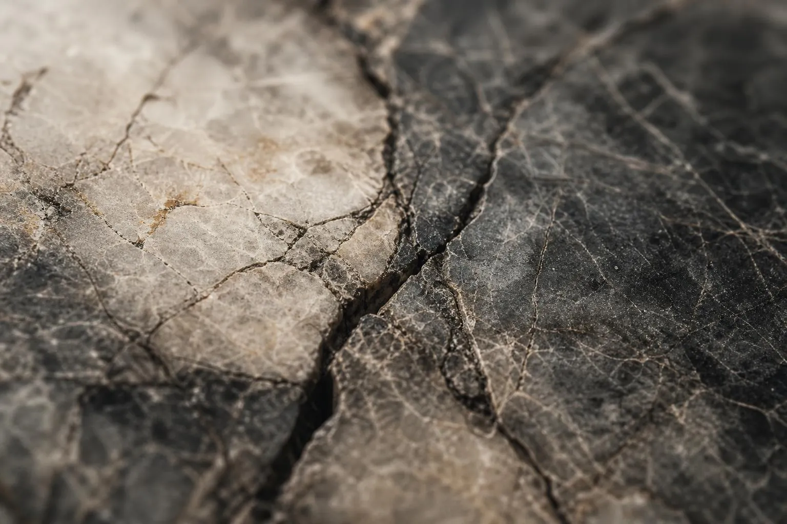 Close-up of aged gray marble with deep veining and subtle fractures in soft light