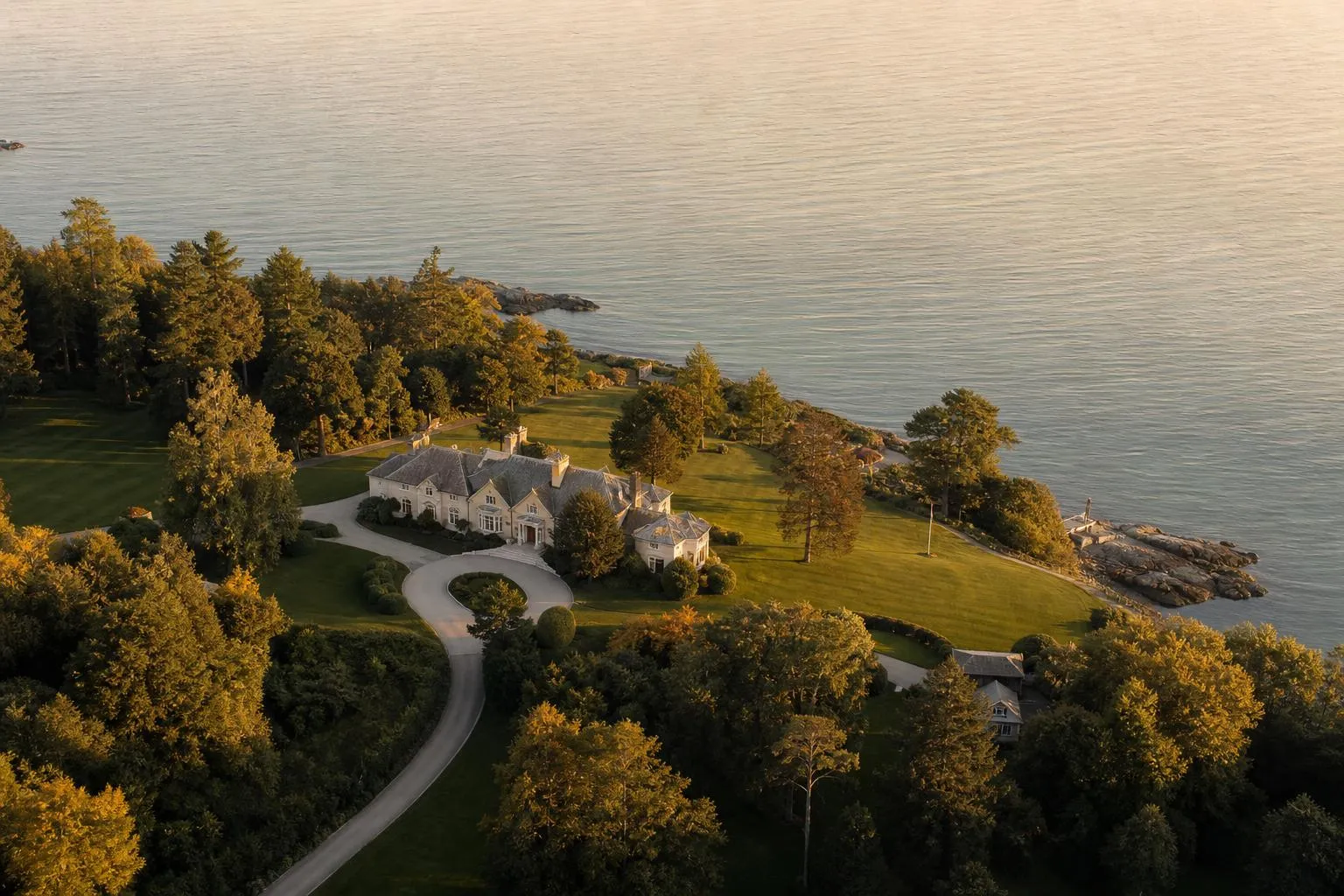 Aerial view of a coastal estate with manicured grounds and private drive at sunset.