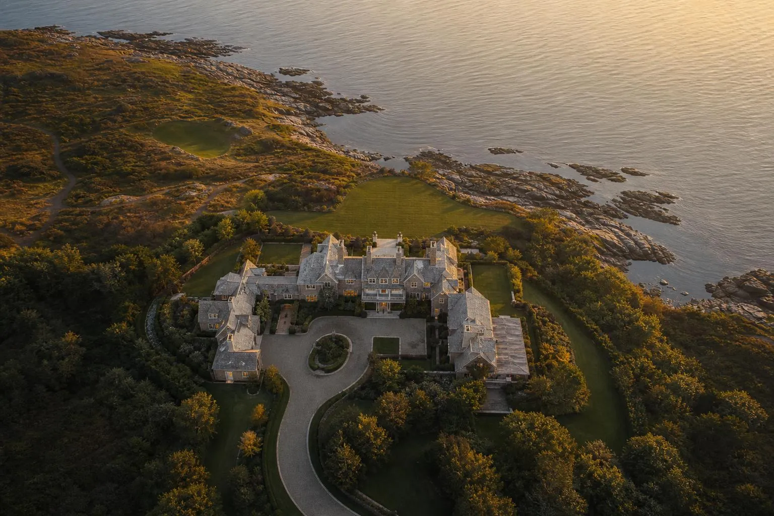 Aerial view of a private coastal estate with manicured grounds at sunset.